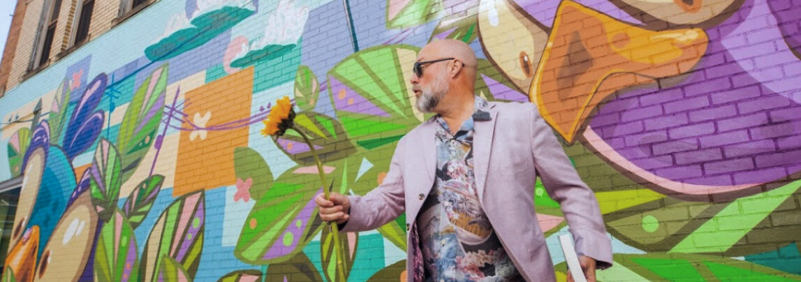 Mike holding a book and a sunflower in an awesome pink blazer.