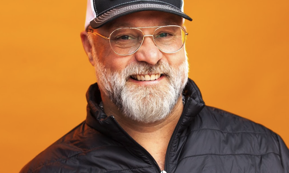 Mike, wearing BIGGBY apparel, smiling in front of an orange backdrop