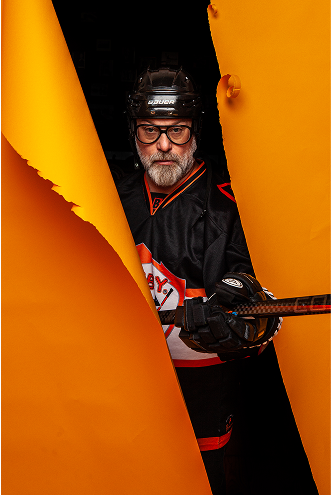 Mike in hockey gear bursting through an orange paper background.